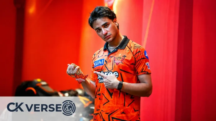 Sunrises Hyderabad Batsman Abhishek Sharma posing in the orange team jersey while holding the gold chain and pointing to the SRH logo.